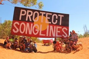 20 people on a red dirt road with a large banner that says protect country