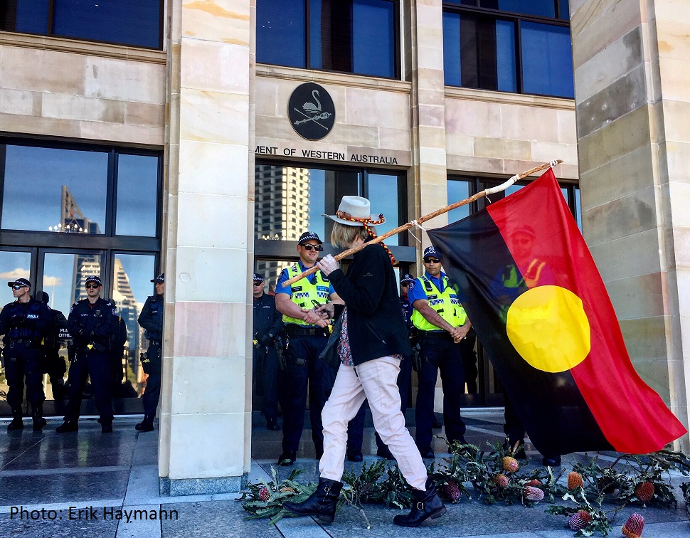 Woman with large Aboriginal flag walks past police