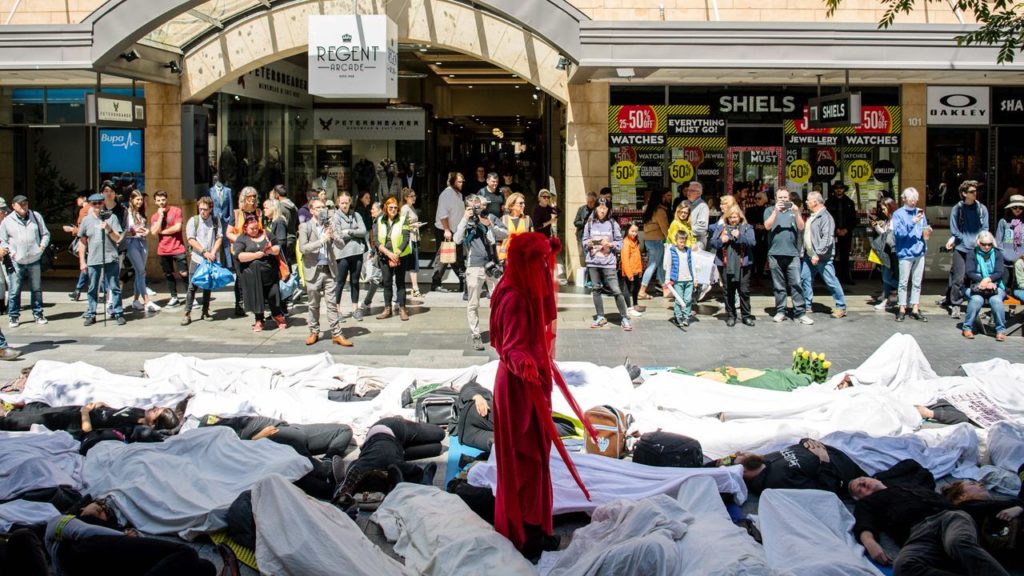Image of a "die in" in a mall, with people in white on the ground and a lone woman in red standing