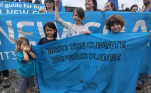Young children hold a banner reading: Take the Climate Defenced Pledge